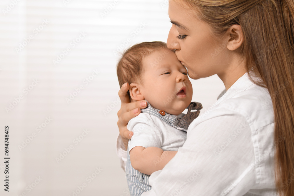 Mother kissing her cute newborn baby indoors, space for text Mother kissing her cute newborn baby indoors, space for text