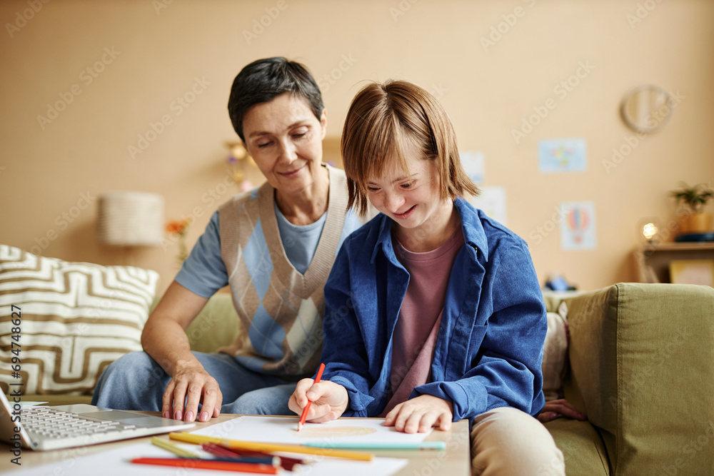 Girl with disability coloring on paper by mother in living room Girl with disability coloring on paper by mother in living room