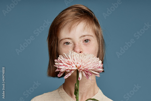 Girl covering mouth with crown daisy against blue background photo