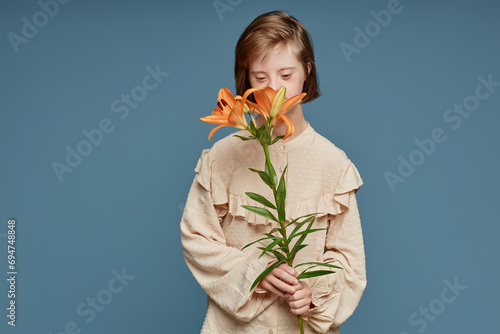Teenage girl smelling orchid flowers standing against blue background photo