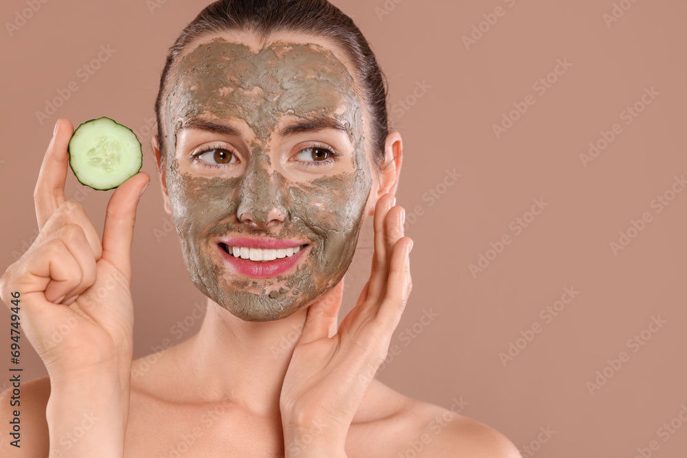 Beautiful woman with clay mask holding piece of cucumber on light brown background. Space for text Beautiful woman with clay mask holding piece of cucumber on light brown background. Space for text