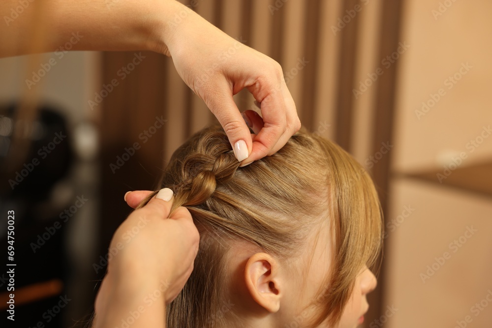 Naklejka premium Professional hairdresser braiding girl's hair in beauty salon, closeup