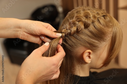 Professional hairdresser braiding girl's hair in beauty salon, closeup