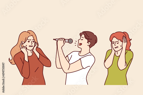 Man sings karaoke poorly due to lack of hearing or voice and forces women to cover ears. Singer holds microphone enjoying visit to karaoke club and annoys people experiencing discomfort.