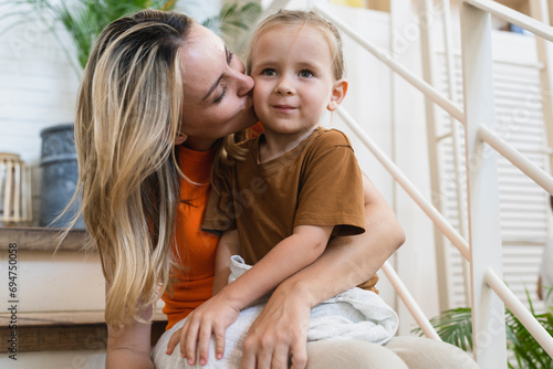 Blond mother kissing cute boy on stairs of house photo