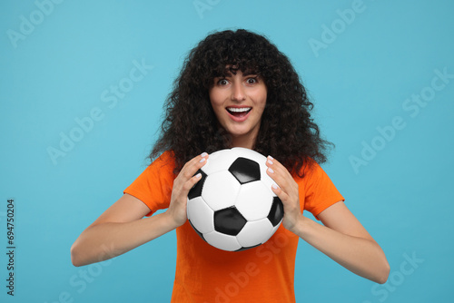 Excited fan holding soccer ball on light blue background © New Africa