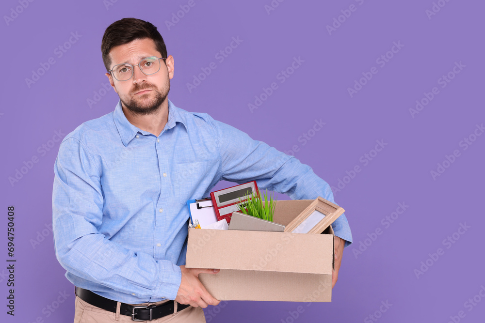 Upset unemployed man with box of personal office belongings on purple background. Space for text Upset unemployed man with box of personal office belongings on purple background. Space for text
