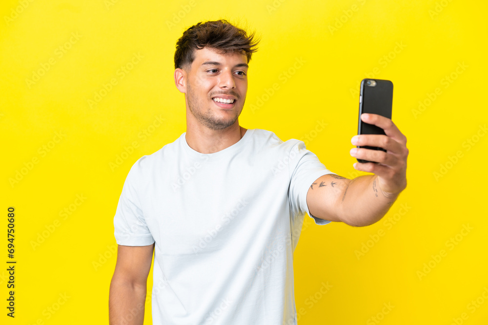 Young caucasian handsome man isolated on yellow background making a selfie with mobile phone Young caucasian handsome man isolated on yellow background making a selfie with mobile phone