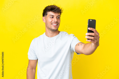 Young caucasian handsome man isolated on yellow background making a selfie with mobile phone