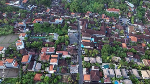 Hotels and restaurants along Bisma street, aerial shot of Ubud town in evening hour, camera fly towards Jl Raya Ubud. Typical view of famous city, small buildings and green trees, villas and resorts photo
