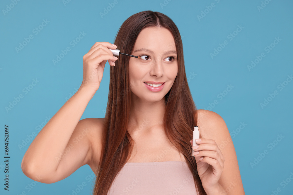 Beautiful woman applying serum onto eyelashes on light blue background Beautiful woman applying serum onto eyelashes on light blue background