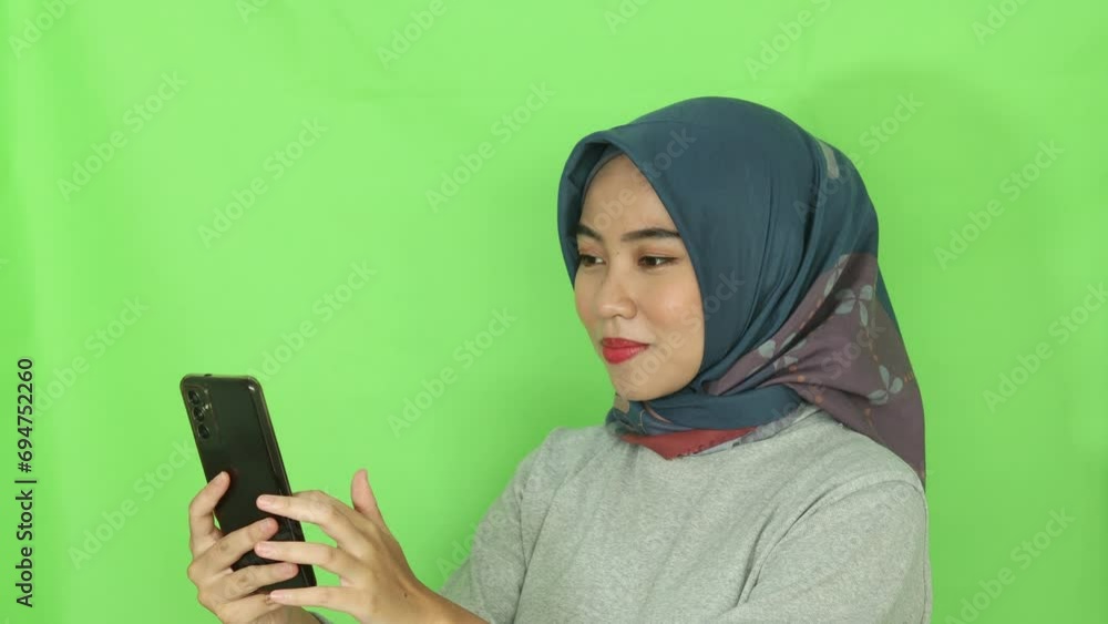 beautiful Asian woman in gray cloth and hijab scrolling a mobile phone screen isolated over green background.
beautiful Asian woman in gray cloth and hijab scrolling a mobile phone screen isolated over green background.