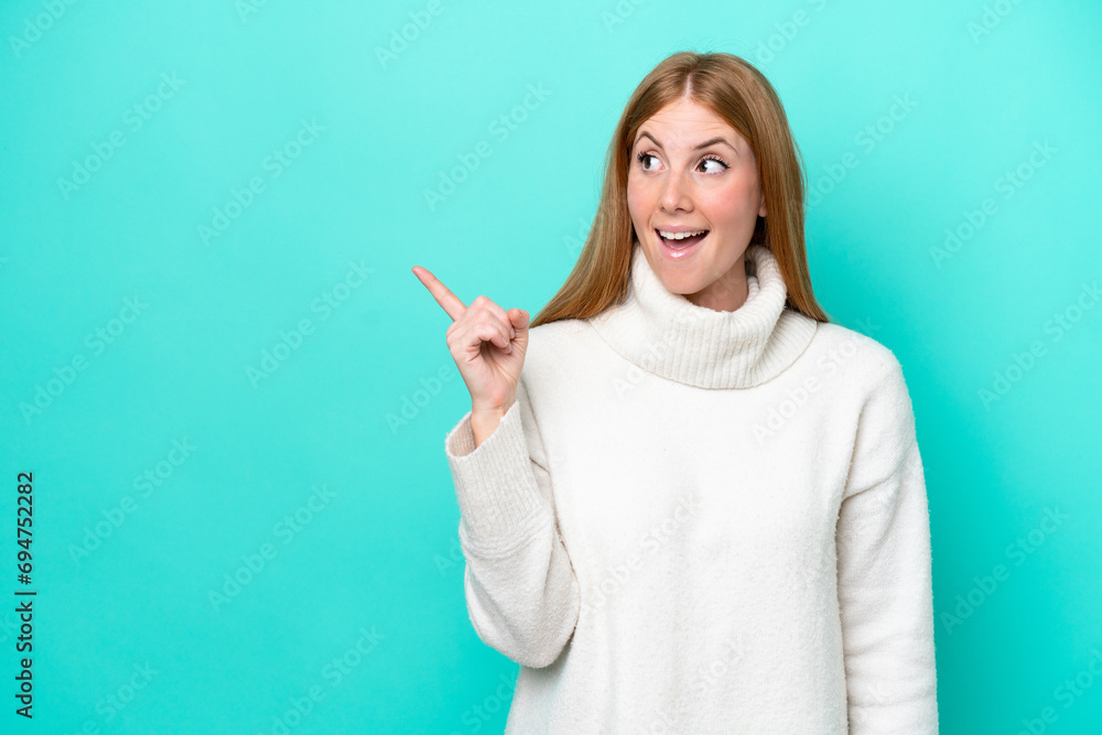 Young redhead woman isolated on blue background intending to realizes the solution while lifting a finger up Young redhead woman isolated on blue background intending to realizes the solution while lifting a finger up