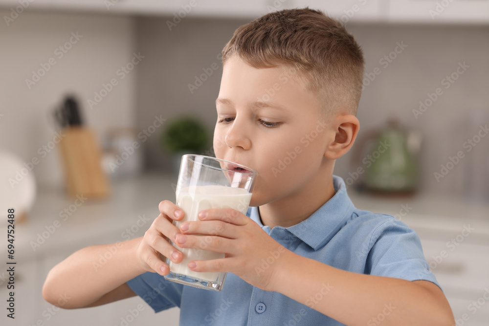 Cute boy drinking fresh milk from glass indoors Cute boy drinking fresh milk from glass indoors