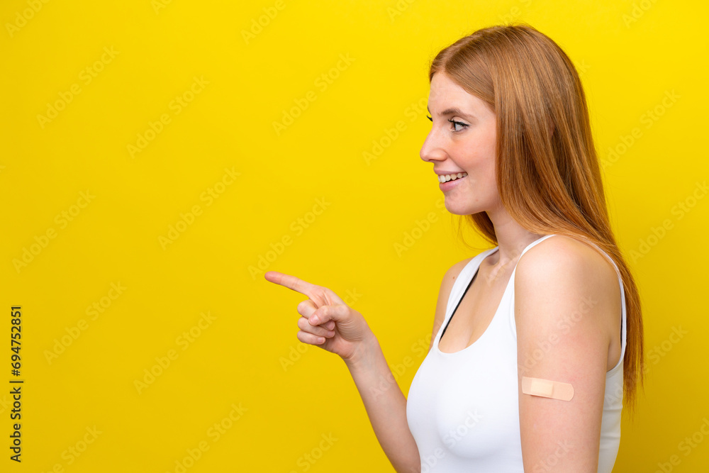 Young redhead woman wearing a band-aids isolated on yellow background pointing to the side to present a product Young redhead woman wearing a band-aids isolated on yellow background pointing to the side to present a product