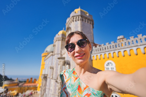 Tourist takes a self-portrait with a smartphone in the background of the Pena Palace and a clear blue sky. Sintra. Lisbon, Portugal. Summer holidays.