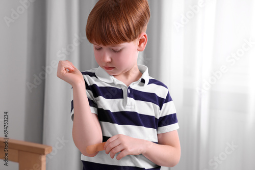 Little boy putting sticking plaster onto elbow indoors