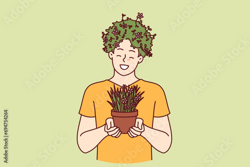 Man with house plant in hands and hairstyle made of grass smiles, enjoying growing indoor flowers and caring for nature. Funny guy enjoys botany and cultivating house plants as hobby.