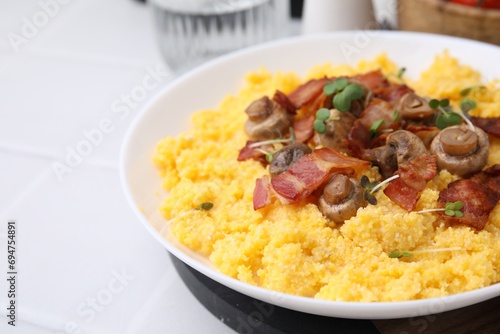 Tasty cornmeal with bacon, mushrooms and microgreens in bowl on white table, closeup. Space for text