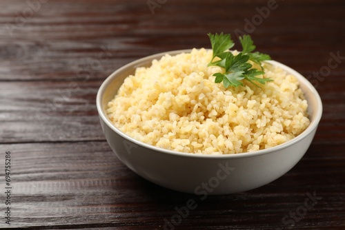 Delicious bulgur with parsley in bowl on wooden table, closeup. Space for text