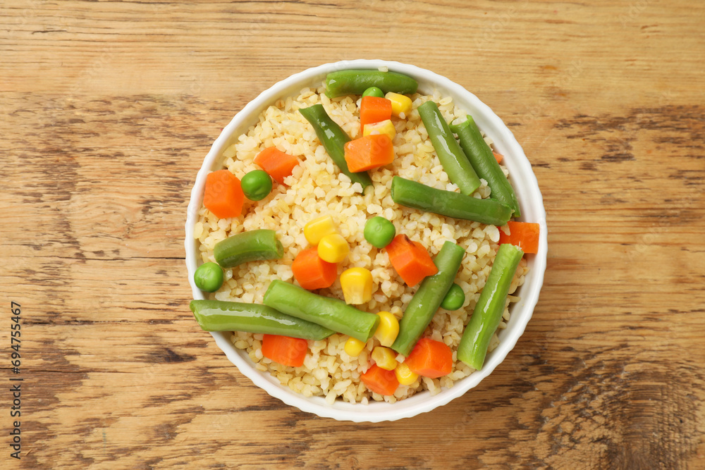 Delicious bulgur with vegetables in bowl on wooden table, top view Delicious bulgur with vegetables in bowl on wooden table, top view
