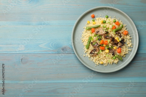 Delicious bulgur with vegetables and mushrooms on light blue wooden table, top view. Space for text photo