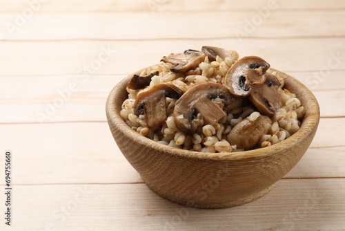 Delicious pearl barley with mushrooms in bowl on wooden table, closeup. Space for text