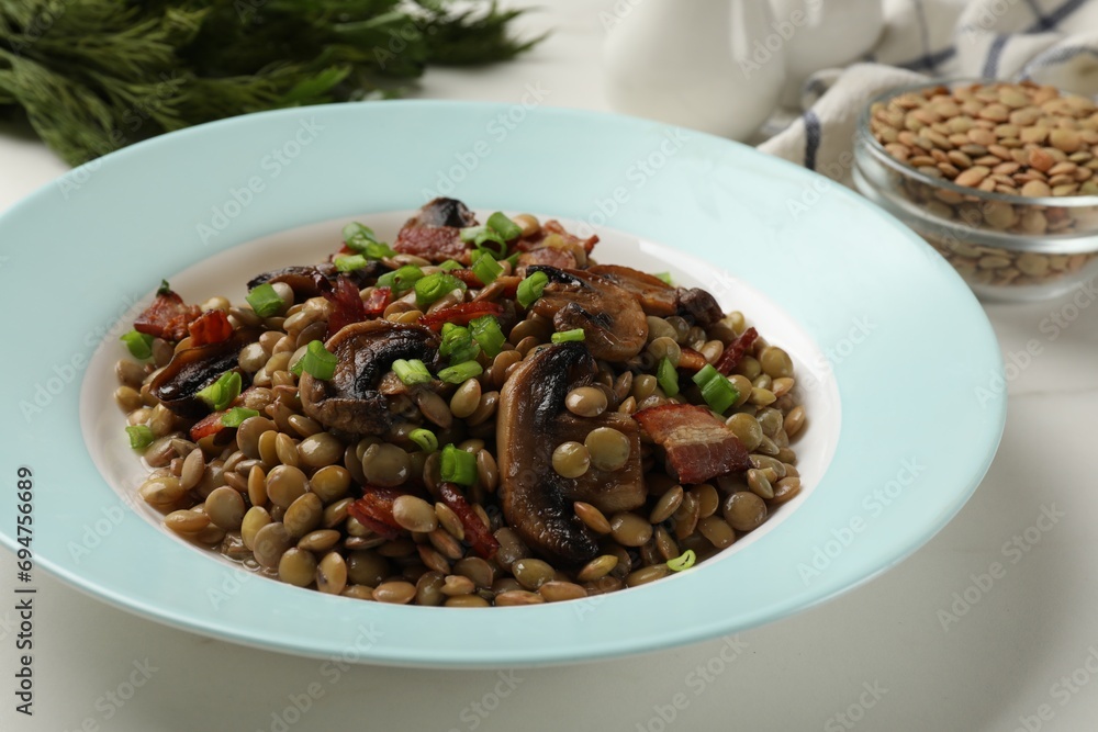 Delicious lentils with mushrooms, bacon and green onion on white table, closeup Delicious lentils with mushrooms, bacon and green onion on white table, closeup