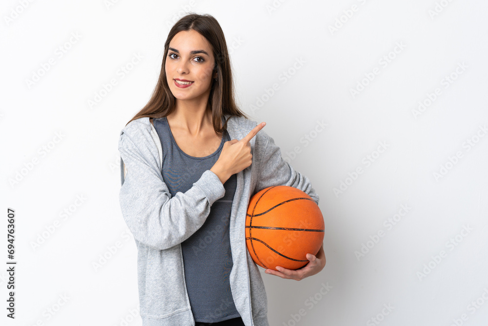 Young woman playing basketball isolated on white background pointing to the side to present a product Young woman playing basketball isolated on white background pointing to the side to present a product