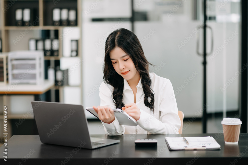 Successful Asian Businesswoman Analyzing Finance on Tablet and Laptop at Office Desk tax, report, accounting, statistics, and analytical research concept.