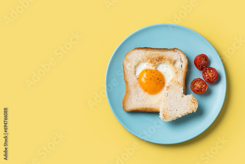 Valentine's Day breakfast with egg with tomatoes, heart shaped and toast bread on yellow background. Top view. Copy space