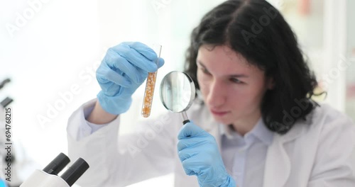 The lab assistant guy looks through the magnifier on the seeds in the flask. Comus suitability for sowing photo