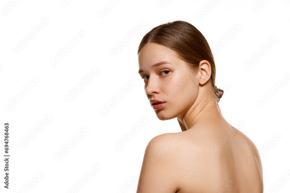 Portrait of young and beautiful brunette woman with perfect smooth skin looks over his shoulder at camera against white studio background. Portrait of young and beautiful brunette woman with perfect smooth skin looks over his shoulder at camera against white studio background.