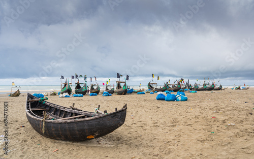 Moody landscape view of traditional wooden fishing boats known as moon boats on beach under cloudy sky, Cox's Bazar, Bangladesh photo