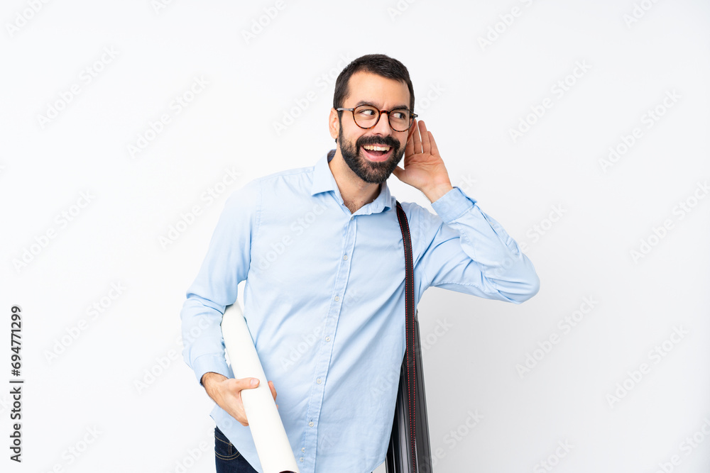 Young architect man with beard over isolated white background listening to something by putting hand on the ear Young architect man with beard over isolated white background listening to something by putting hand on the ear