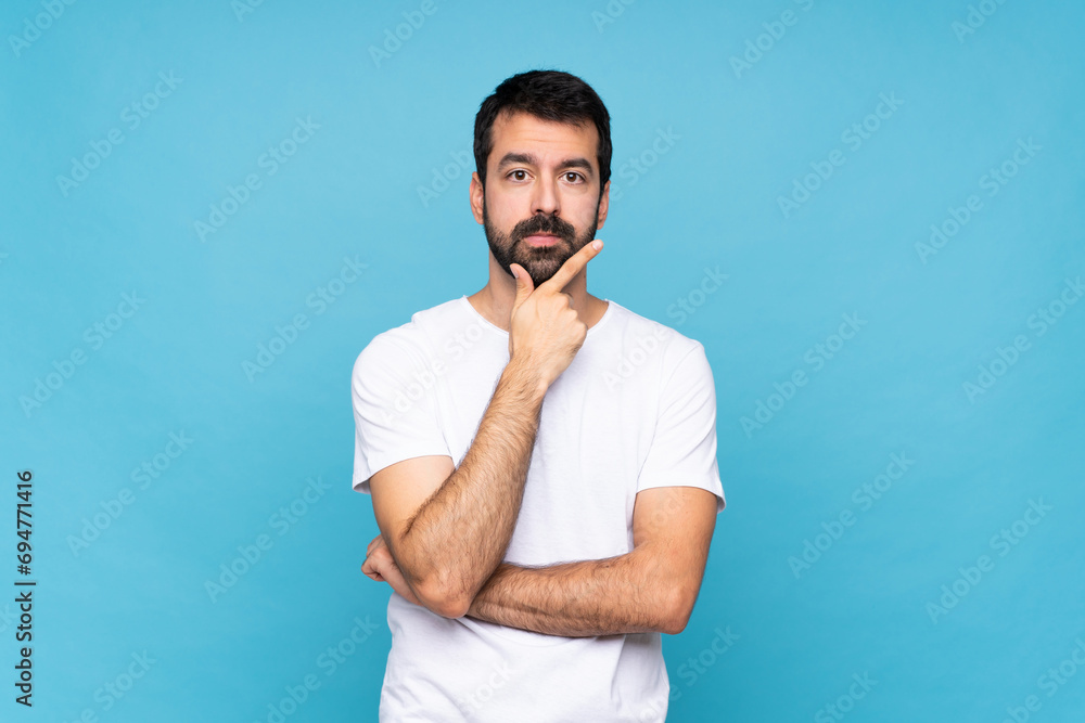 © luismolinero - Young man with beard  over isolated blue background thinking