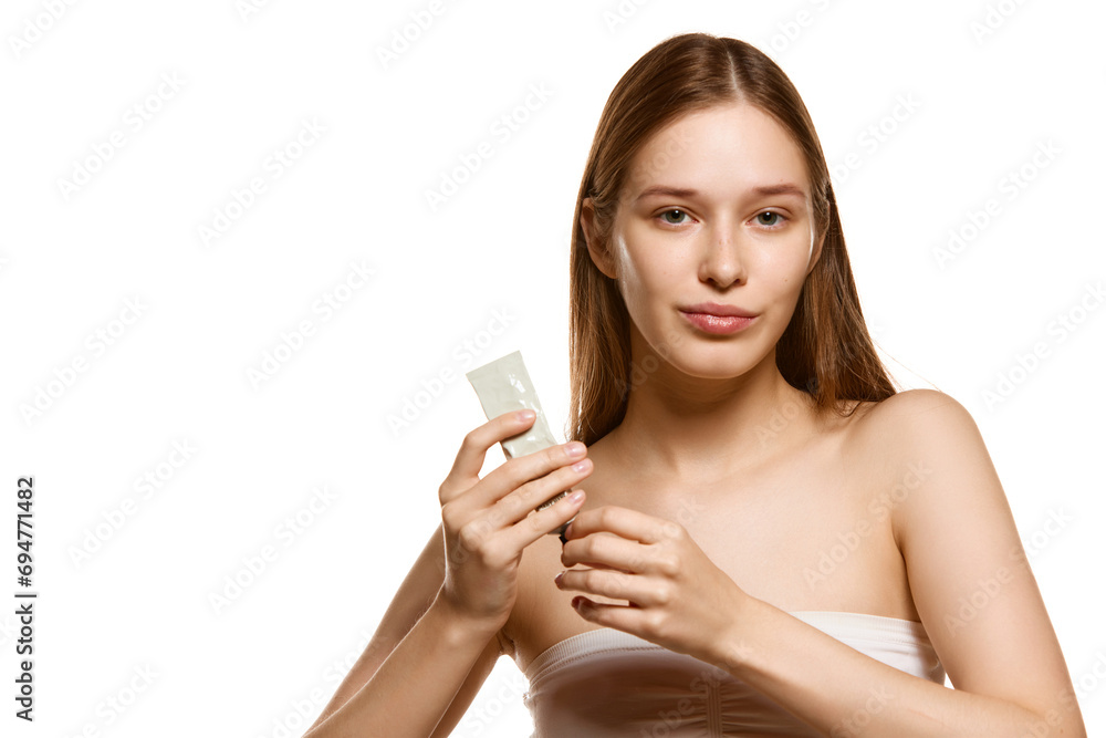 Portrait of pretty young woman looking at camera and holds cream tube to facial skin to maintain its healthy and radiant appearance. Portrait of pretty young woman looking at camera and holds cream tube to facial skin to maintain its healthy and radiant appearance.