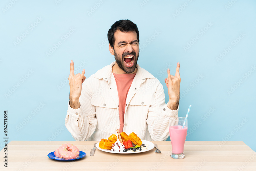 Man at a table having breakfast waffles and a milkshake making rock gesture Man at a table having breakfast waffles and a milkshake making rock gesture