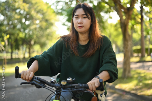Happy young Asian woman riding a bicycle through the city park. Active urban lifestyle concept. © Prathankarnpap