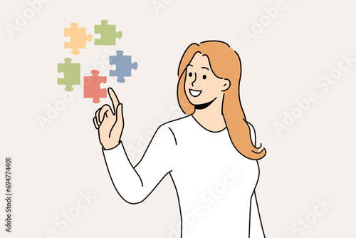 Confident woman doing brainstorming touching with finger flying puzzles symbolizing business task that requires solution. Girl with smile solves complex business problem on behalf of manager. photo