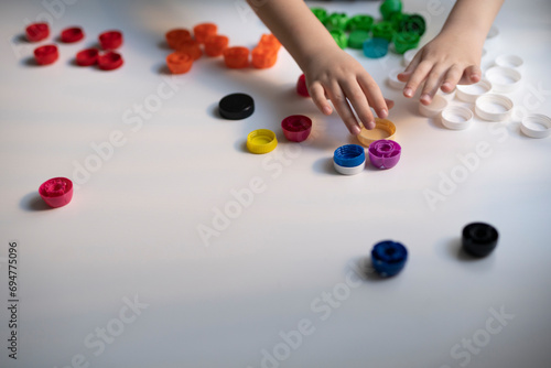 child separates multi-colored caps on a white background. banner, background. separate waste collection. recycling fee. ecology. selective focus.