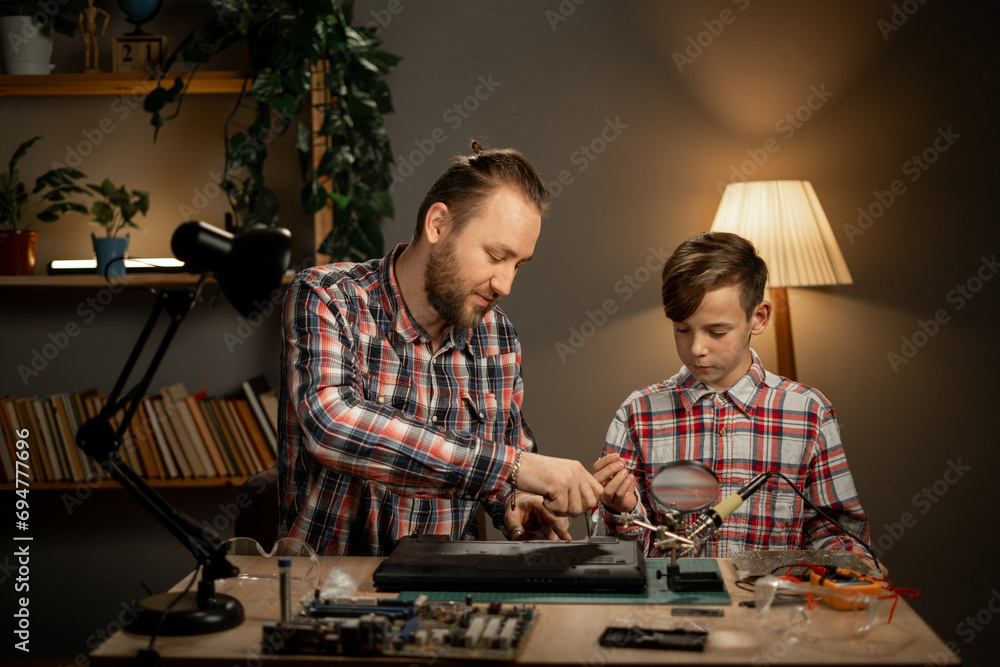 A father teaches his son how to repair a broken laptop and a damaged hard drive, a hobby for children and parental help - obrazy, fototapety, plakaty 