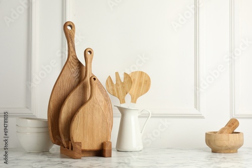 Wooden cutting boards, kitchen utensils and dishware on white marble table