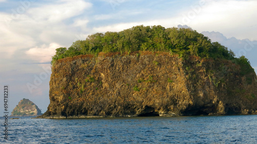 Rocky island in the sea. An island with a steep cliff covered with green trees in the tropical sea.