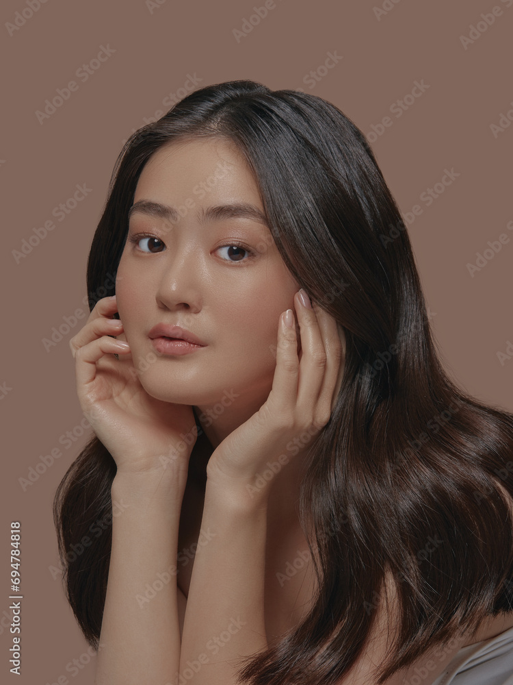Beautiful portrait of an attractive japanese sensual young woman with a healthy clean skin and long brunette hair, touching her face standing isolated on a beige background Beautiful portrait of an attractive japanese sensual young woman with a healthy clean skin and long brunette hair, touching her face standing isolated on a beige background