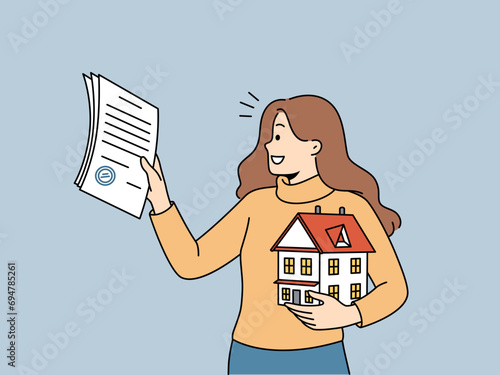 Woman realtor helps people in purchasing real estate and holds mortgage contract and model of house in hand. Realtor girl smiles, rejoicing at selling house and receiving percentage for work.