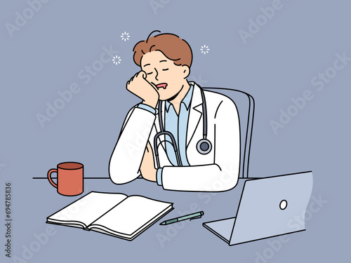 Sleeping man doctor sits at desk with computer and papers after difficult day at work. Guy doctor in white coat needs rest after long absence of vacation and overload when performing medical tasks.