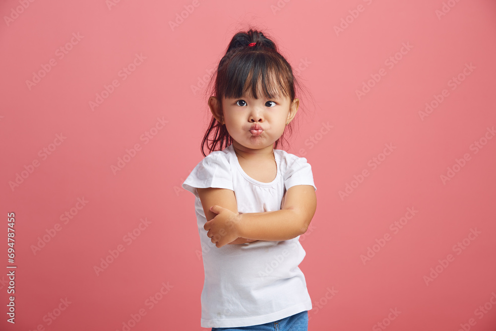 Offended little asian girl with insulted expression, scowls face, stick out lips in discontent, has a negative mood, dressed in white t shirt,crossed hands in front of her poses over pink background. Offended little asian girl with insulted expression, scowls face, stick out lips in discontent, has a negative mood, dressed in white t shirt,crossed hands in front of her poses over pink background.