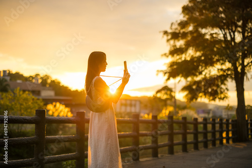 Woman use mobile phone to take photo under sunset