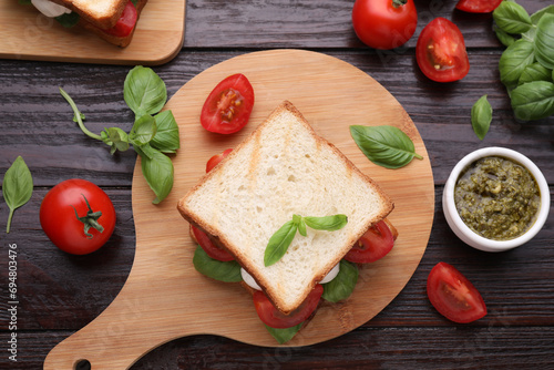 Delicious Caprese sandwich with mozzarella, tomatoes, basil and pesto sauce on wooden table, flat lay